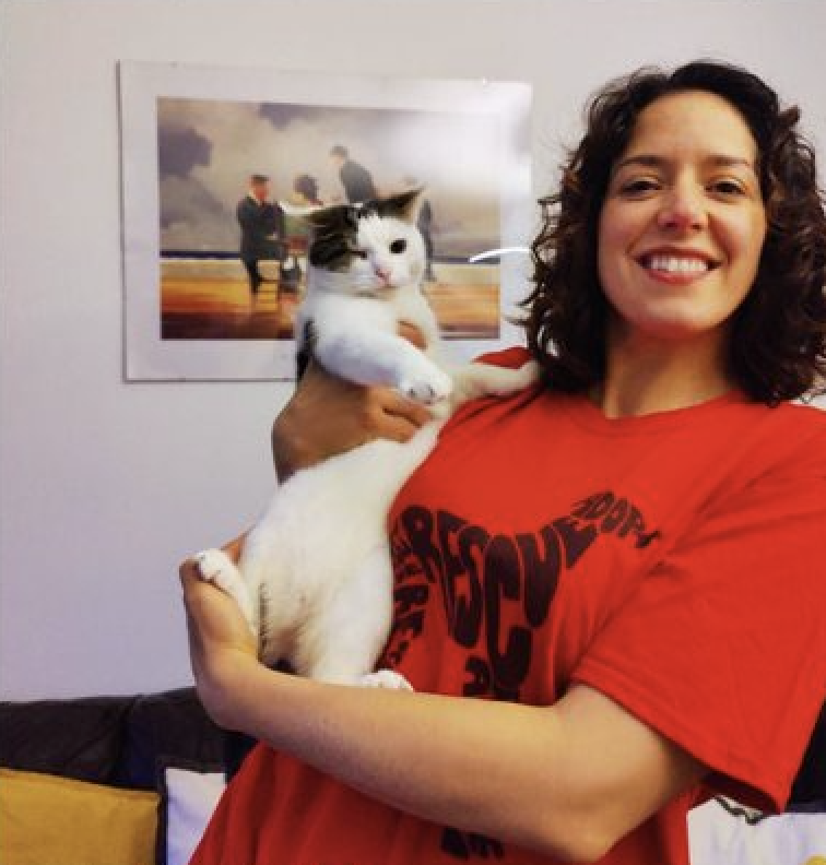 A photo of Paws2Rescue team member Anca wearing a red t-shirt and smiling while holding a black and white cat